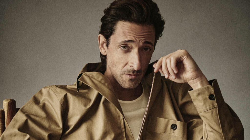 Adrien Brody calm introspective portrait tan jacket soft lighting muted wallpaper background