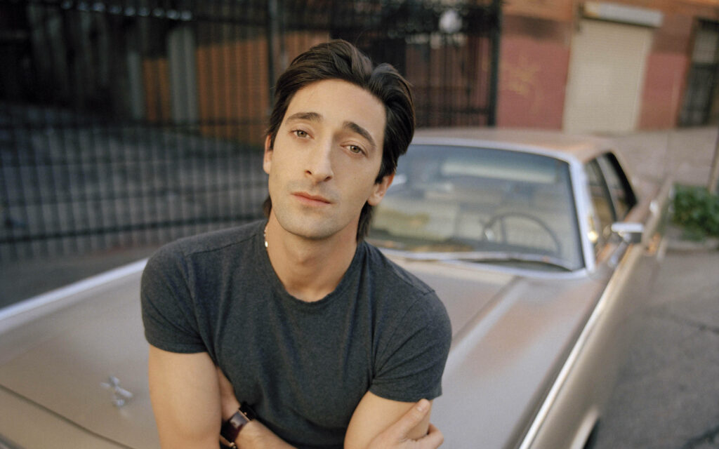 Adrien Brody leaning on vintage car relaxed street timeless wallpaper background scene