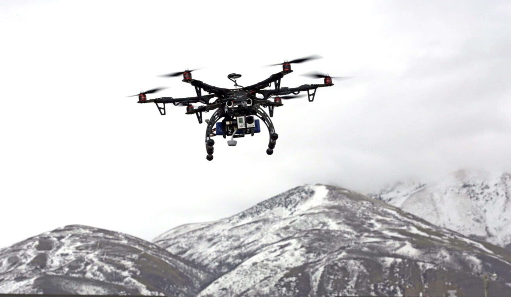 High-tech drone hovering over snow-covered mountains under cloudy sky showcasing aerial innovation Wallpaper