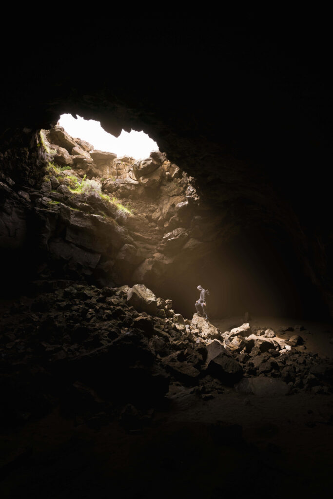 Lone Figure in Dim Cave: Sunlight Through Rocks Creates Adventure Wallpaper