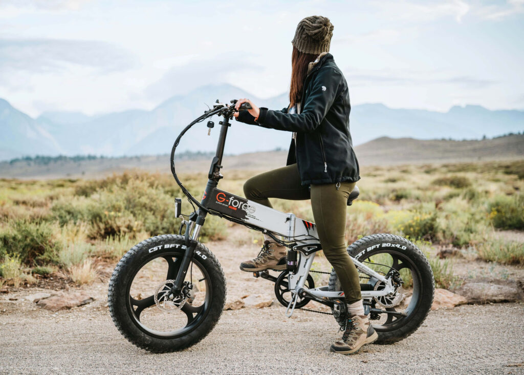 Woman riding rugged G-force electric bike off-road with mountains under overcast sky outdoors Wallpaper