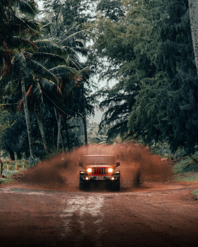 Red Jeep Wrangler Splashing Through Tropical Muddy Path Wallpaper