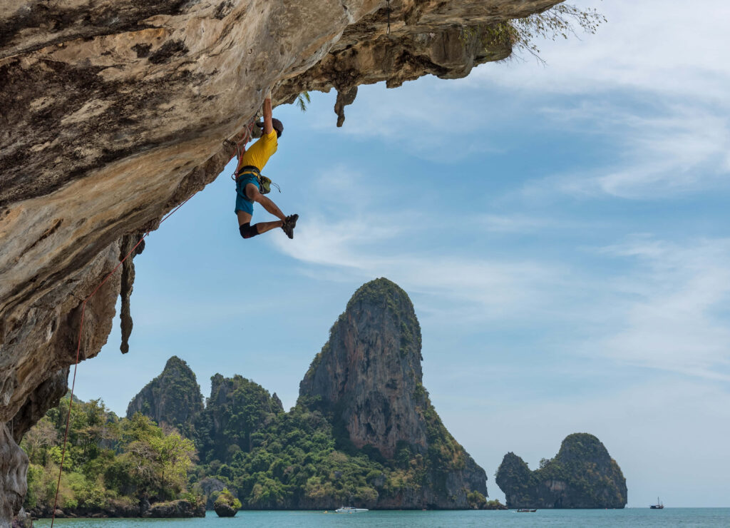 Daring climber free climbing rugged limestone cliff above blue sea with islands and clear sky Wallpaper