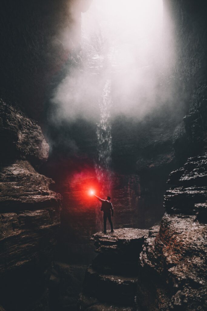 Man with flare stands on cave stones under natural light beams misty atmosphere adventure scene Wallpaper