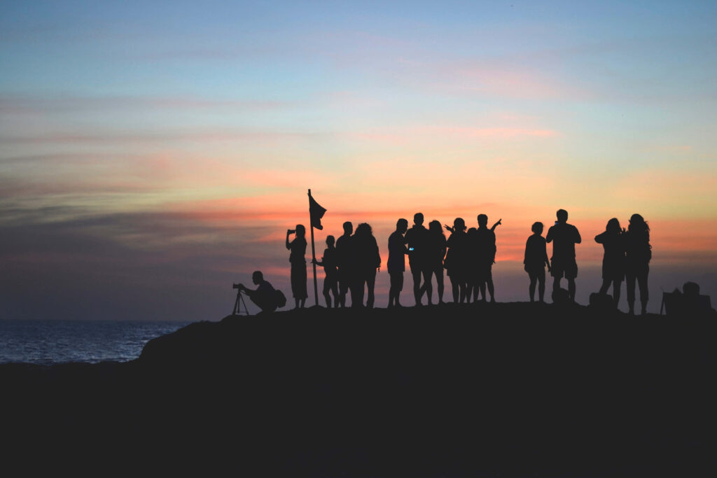 Sunset Silhouettes: Friends and Flag Overlooking Water Wallpaper