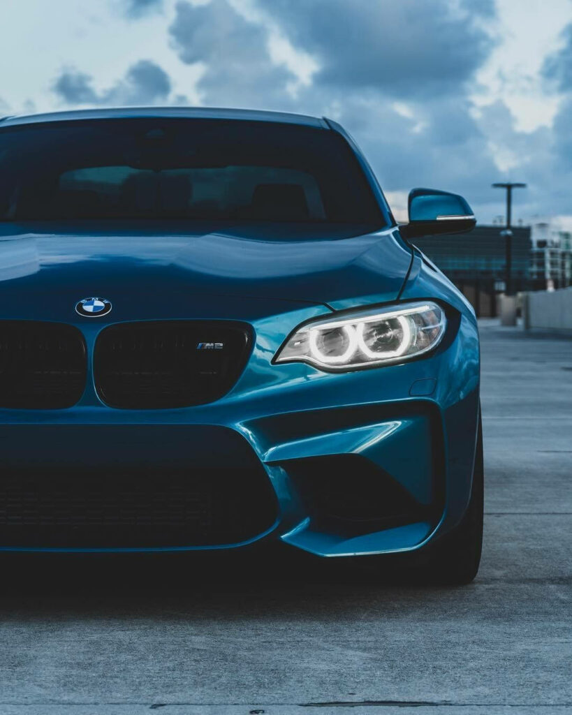 Aegean Blue BMW M2 on urban rooftop with bold grille sleek headlights dramatic sky background Wallpaper