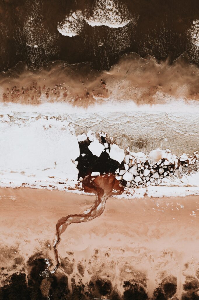 Aerial view of coastal icy formations flowing into sea water channels on a sandy beach Wallpaper