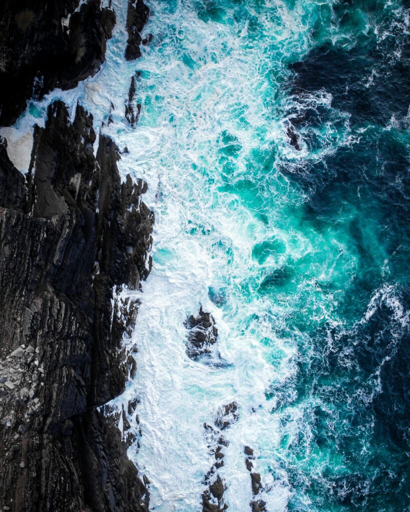 Aerial view of turquoise waves crashing on jagged coastal rocks with foamy white surf Wallpaper