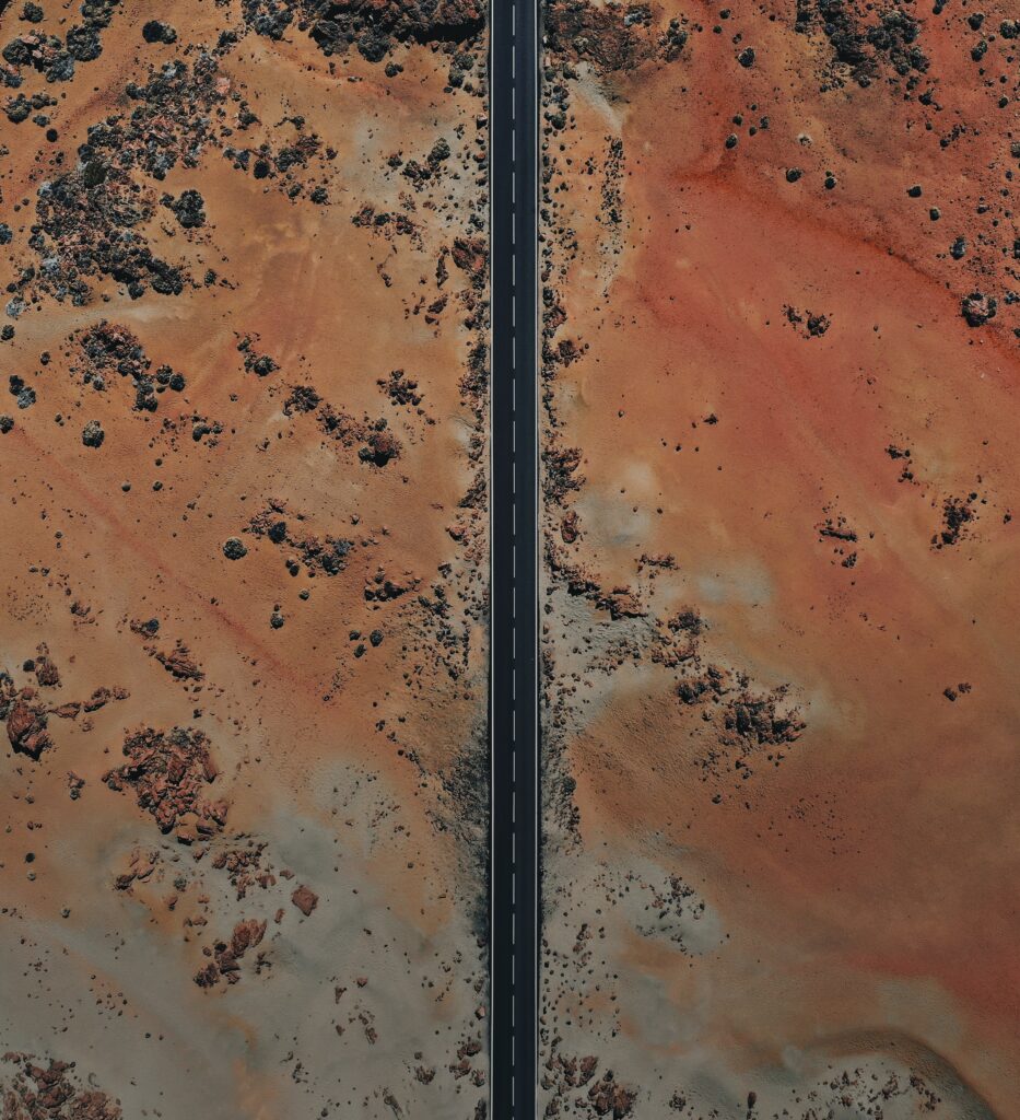 Aerial view of straight desert road with vivid orange sandy terrain and scattered stones wallpaper