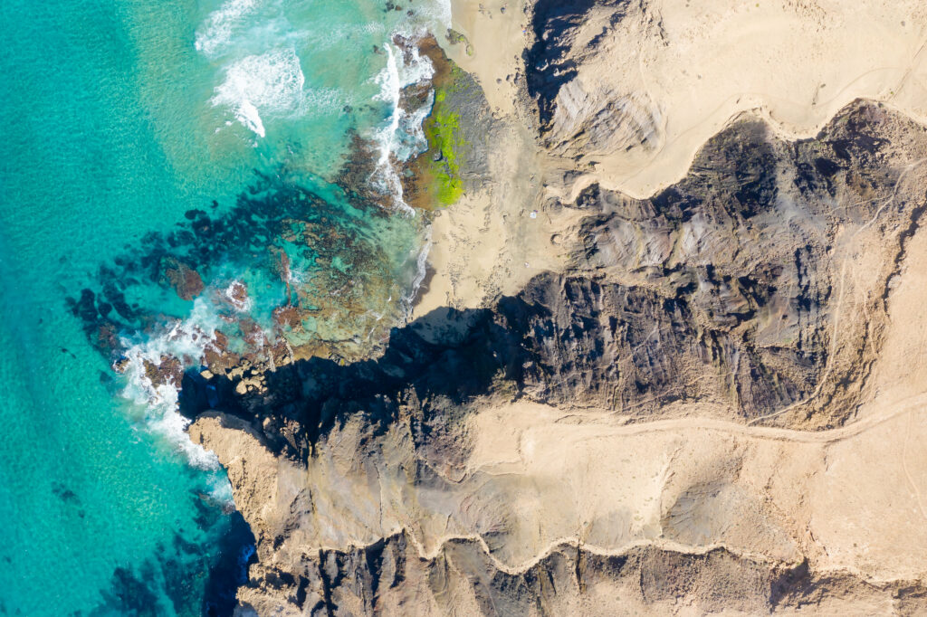 Aerial view of island with turquoise sea rocky terrain and sunlit sandy coastal patterns wallpaper