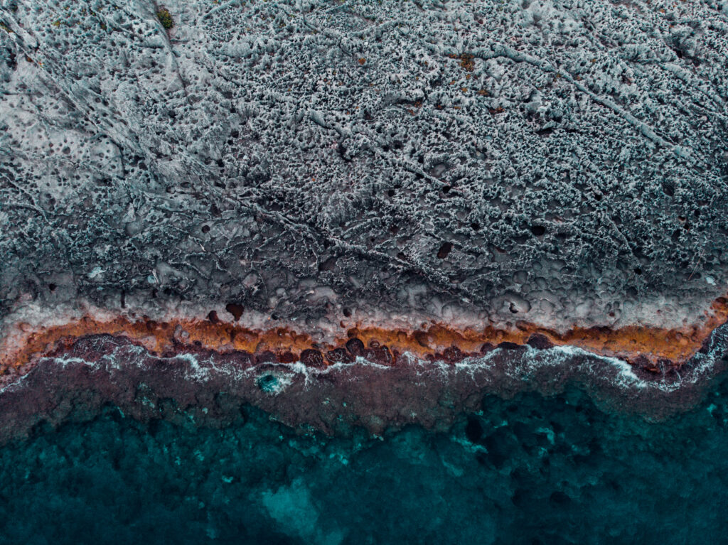Aerial ocean coastline with deep blue water meeting rugged ribbed stone textured shore background Wallpaper
