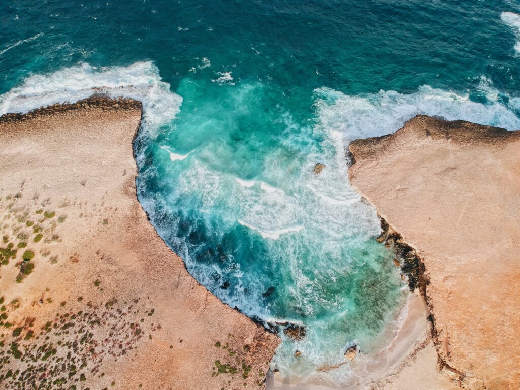 Aerial view of vibrant ocean surf crashing between sandy cliffs with foamy waves coastline Wallpaper