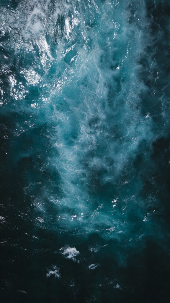 Aerial view of ocean waves with deep blue turquoise hues textured water and white splashes wallpaper