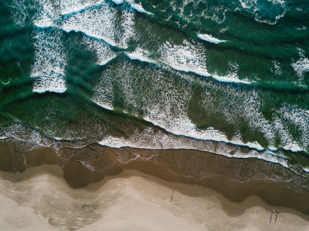 Aerial view of powerful surf and foamy waves rolling onto sandy beach with deep green ocean Wallpaper