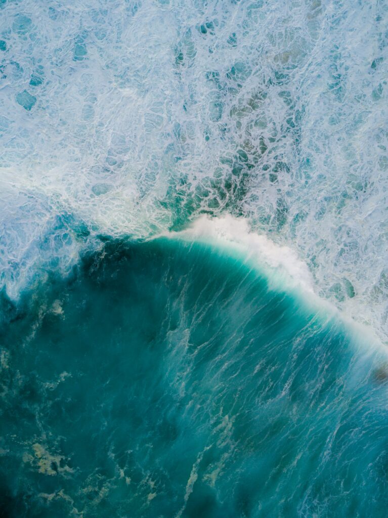 Aerial view of ocean waves crashing with deep teal water and white foamy surf wallpaper background