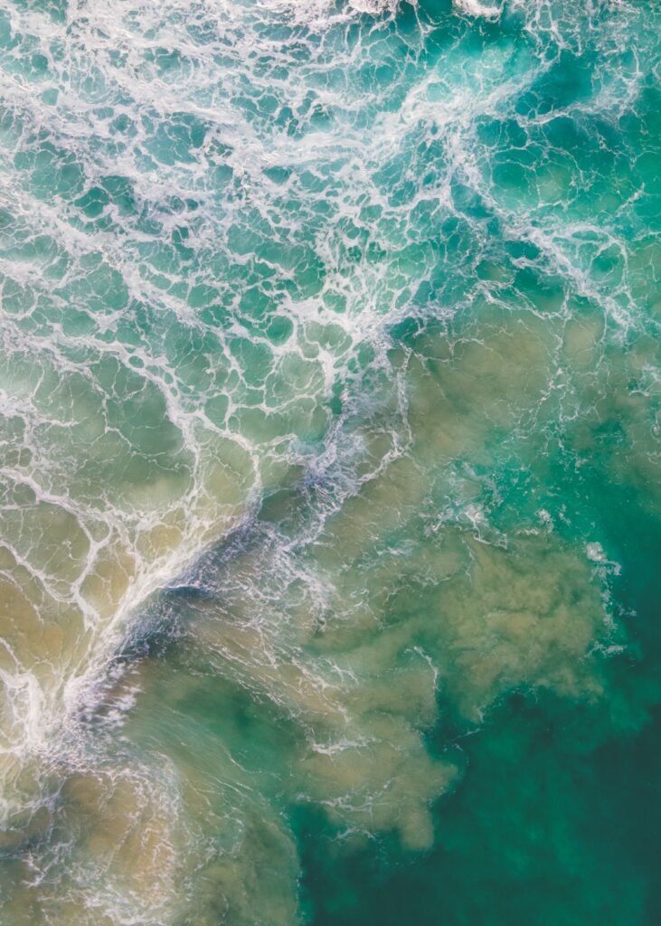 Aerial view of turquoise ocean waves with swirling white currents creating abstract patterns Wallpaper