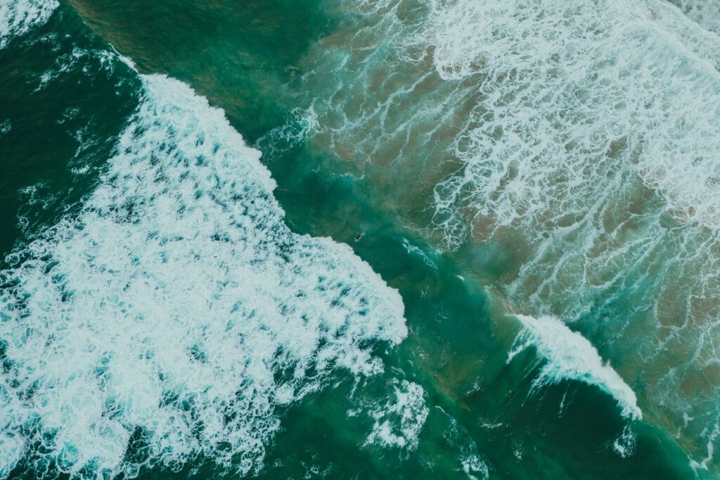 Aerial view of ocean waves crashing in vibrant turquoise and deep blue sea wallpaper background
