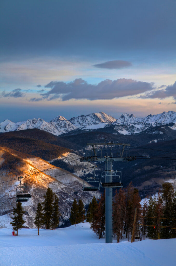Aerial lift over snowy winter slopes with majestic mountains in soft evening light wallpaper background
