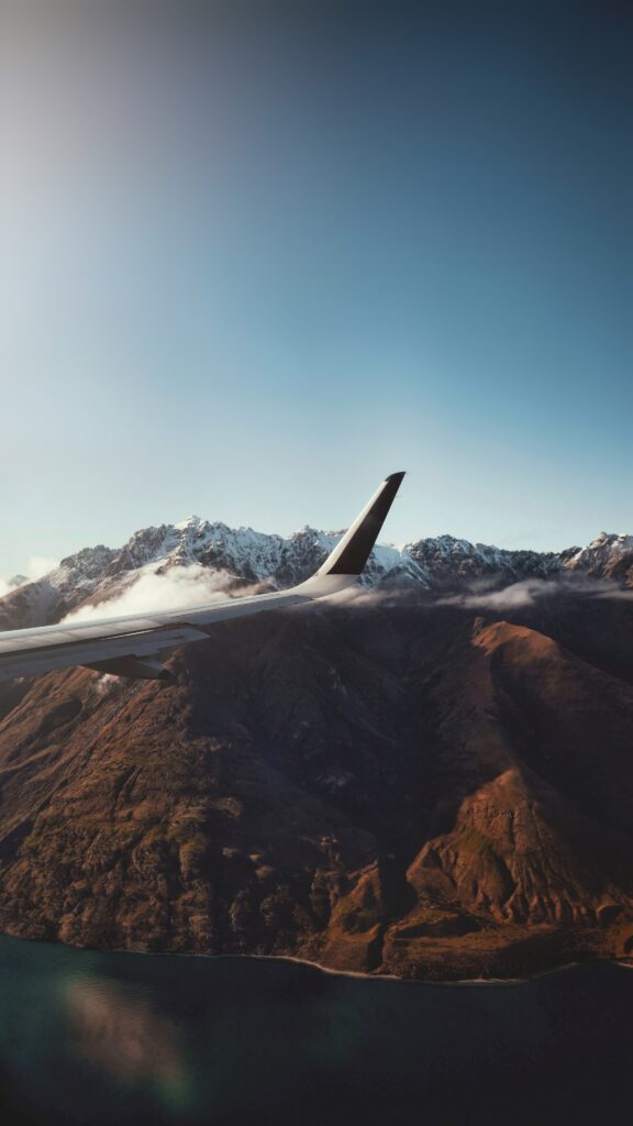 Aerial view of airplane wing above snow-capped mountains under clear blue sky wallpaper background