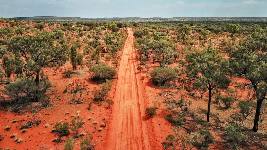 Aerial view of Australian Outback red dirt road through rugged bushland under open sky wallpaper