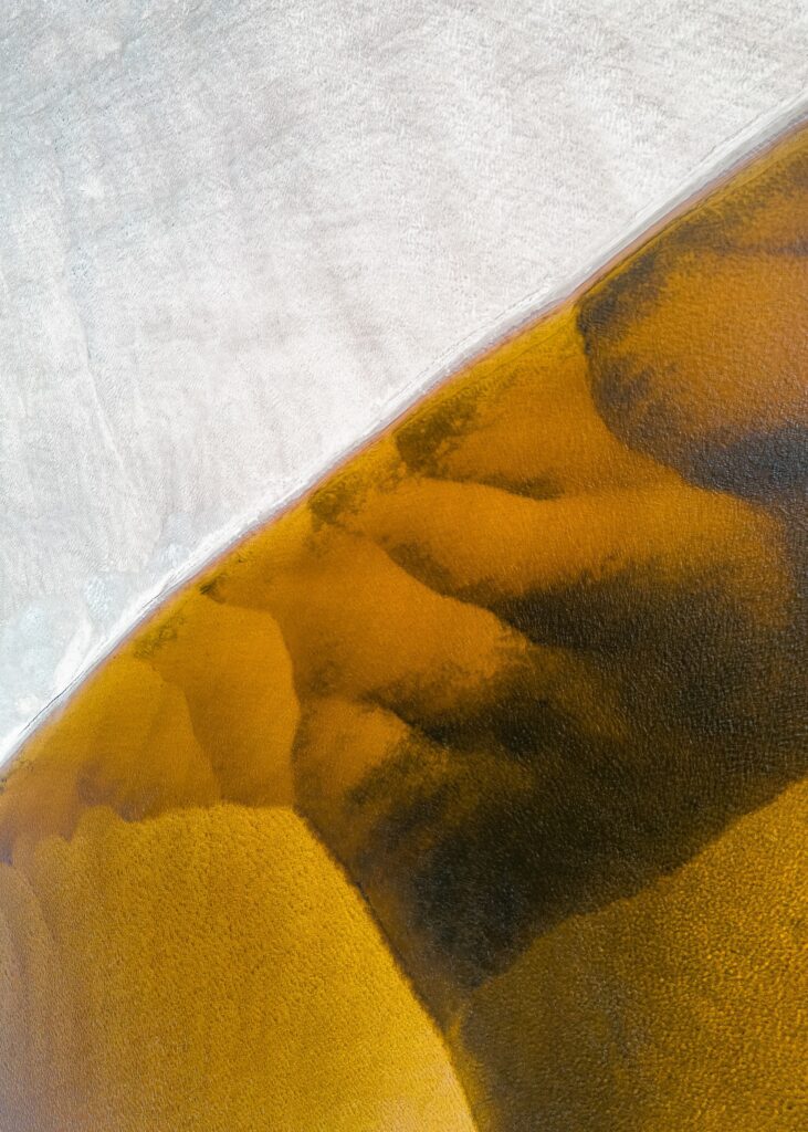 Aerial view of golden sandy beach meeting clear shallow water with natural abstract patterns Wallpaper