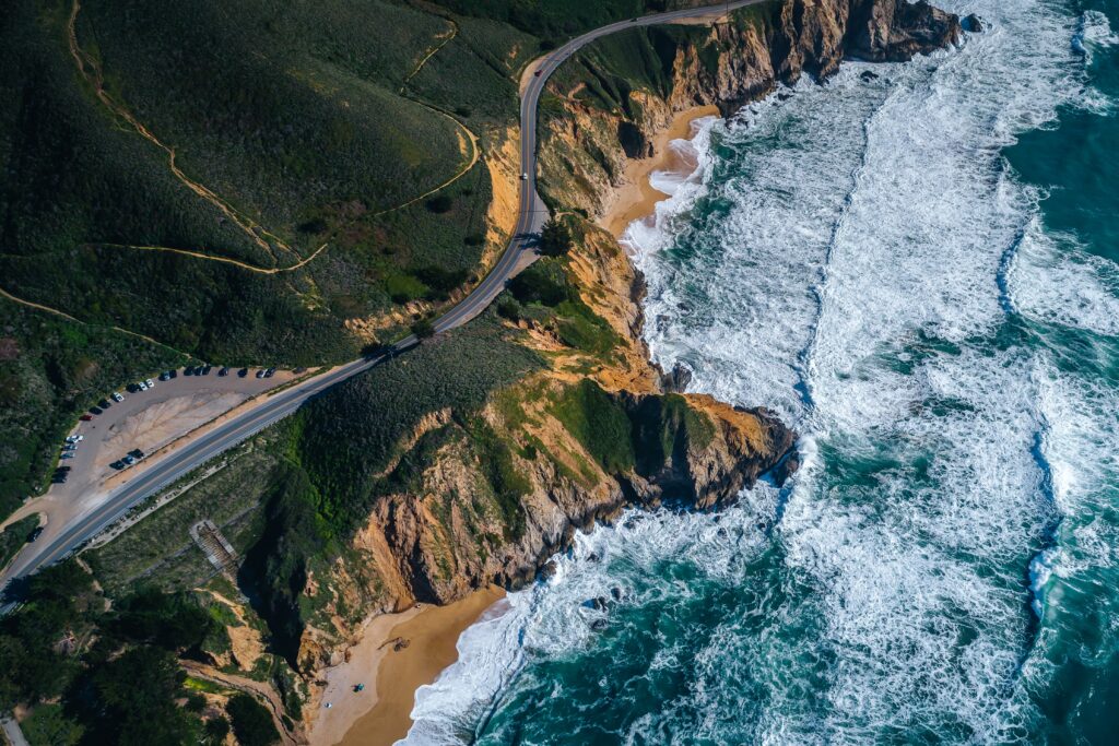 Aerial view of rocky cliffs turquoise waves golden beaches and winding coastal road landscape wallpaper
