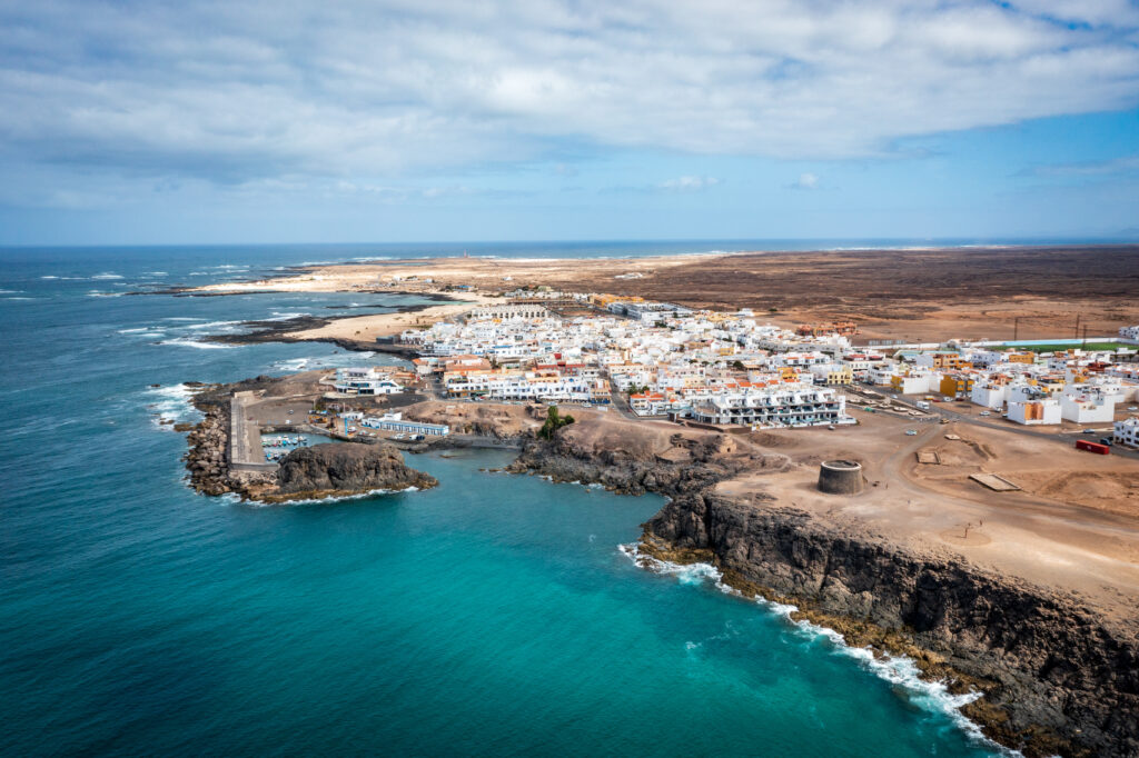 Aerial view of coastal island village with white buildings turquoise sea rugged cliffs wallpaper background