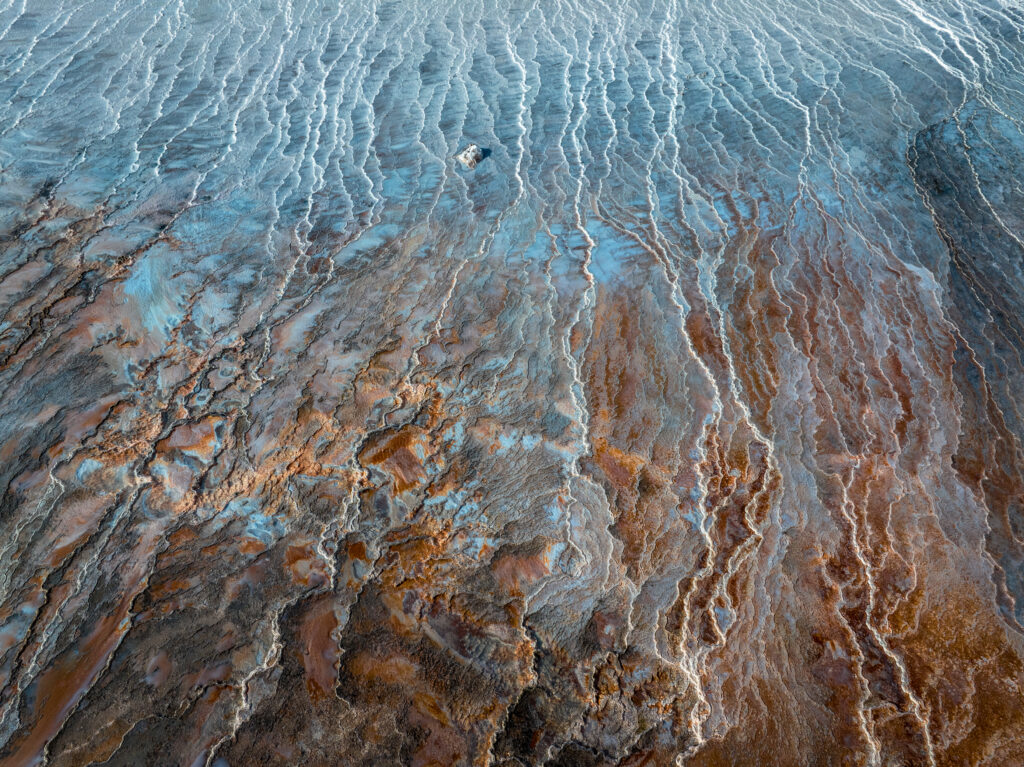 Aerial view of coastal shoreline with blue water and rocky brown textures in abstract patterns Wallpaper
