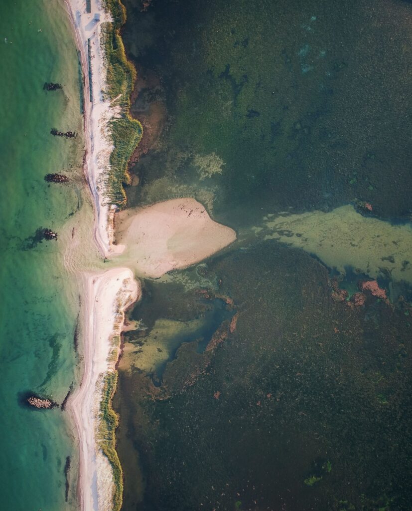 Aerial view of coastline with soft sand and vibrant green blue water showing natural shore patterns Wallpaper