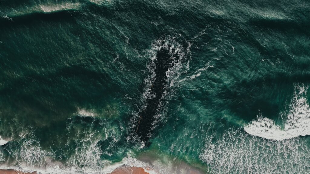 Aerial view of rugged breakwater with powerful sea waves crashing in deep green and blue water Wallpaper