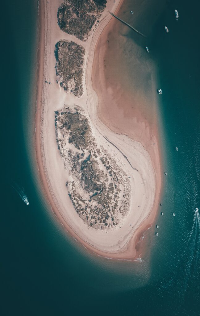 Aerial view of crescent sandy island with boats in deep blue ocean tranquil maritime scenery wallpaper