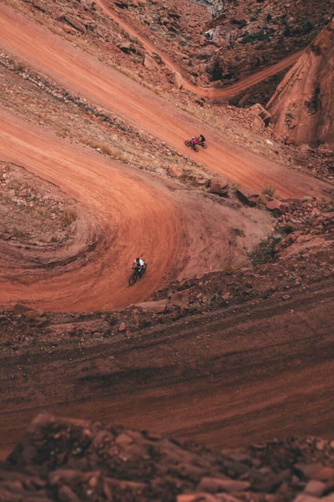 Aerial view of two cyclists riding winding red dirt roads in rugged terrain adventurous movement Wallpaper