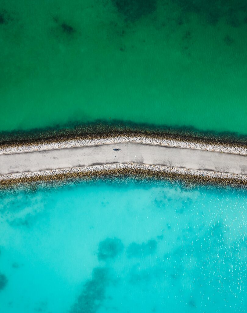 Aerial view of dam road dividing vibrant green and turquoise blue waters natural wallpaper background