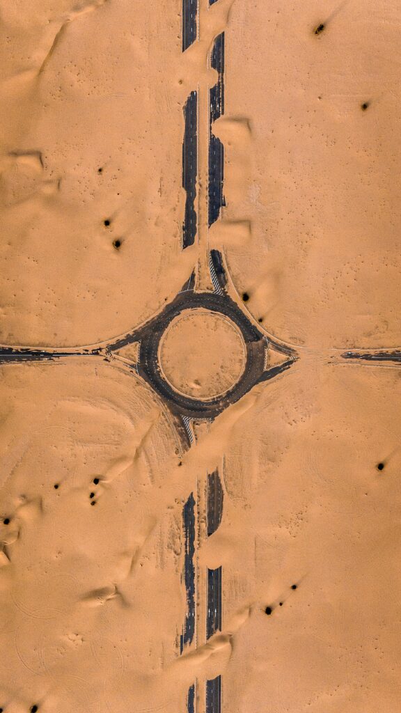Aerial view of desert roundabout with dark asphalt roads cutting through golden sand patterns Wallpaper