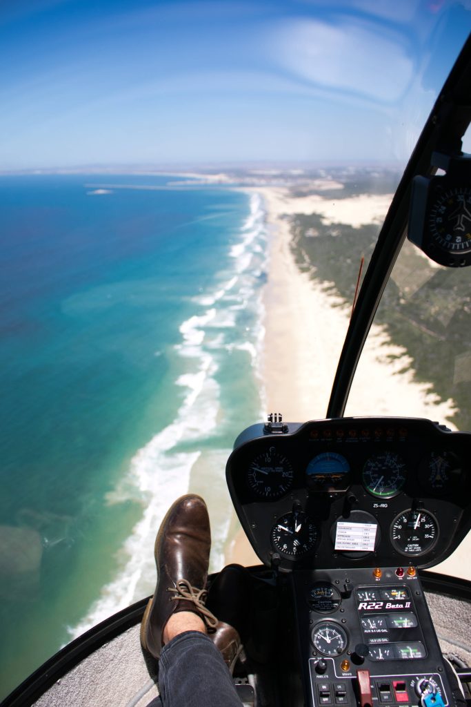 Aerial view from Robinson R22 Beta II cockpit over turquoise waves and sandy coastline beach Wallpaper
