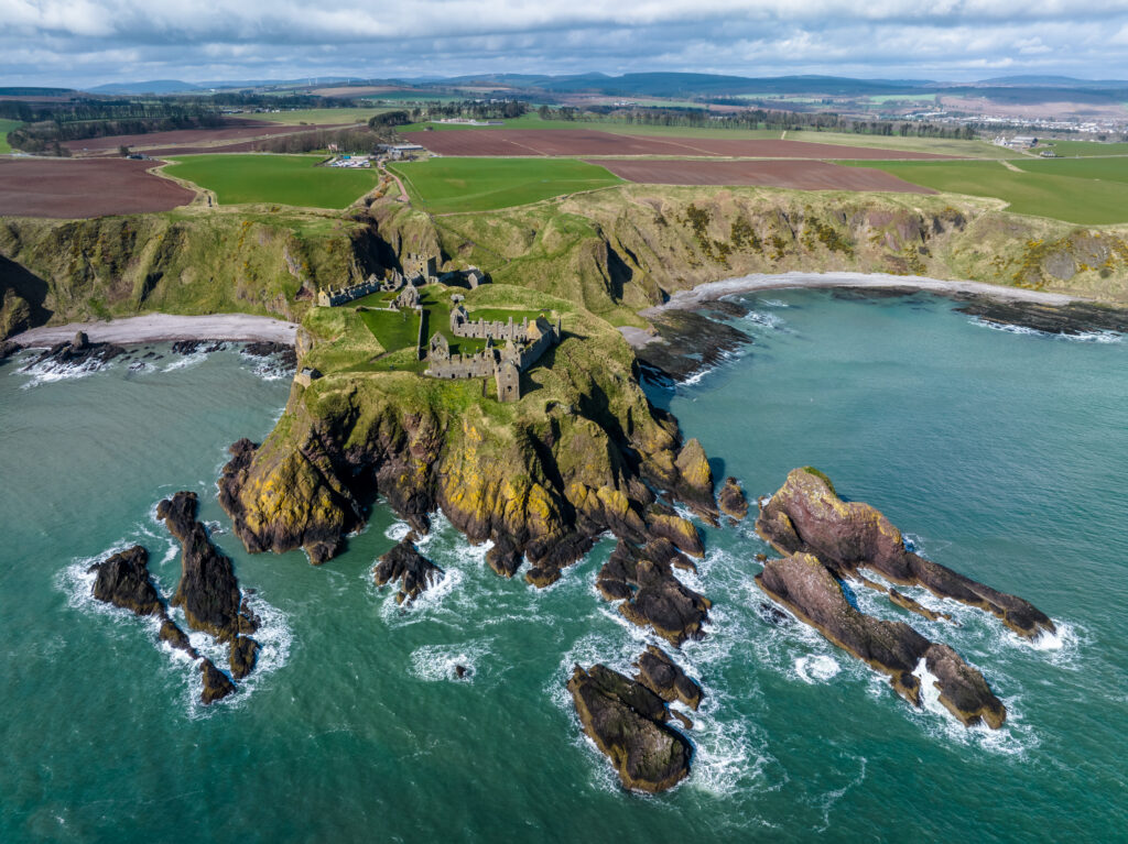 Aerial view of island cliff fortress with lush fields rugged rocks and churning sea background Wallpaper