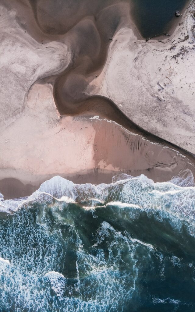 Aerial view of ocean waves meeting sandy shore with natural tidal patterns and coastline relief Wallpaper