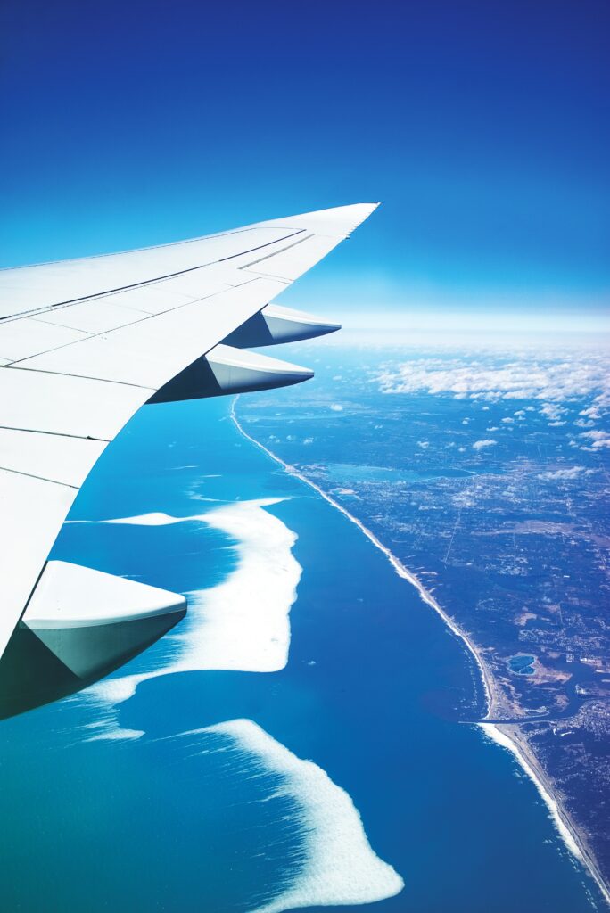 Aerial view from plane wing over city coastline and deep blue ocean under clear sky wallpaper background