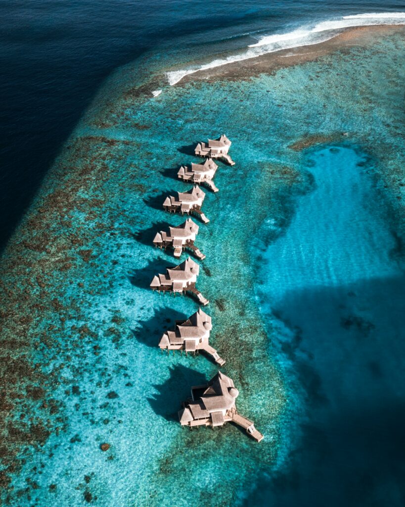Aerial view of overwater bungalows above turquoise ocean surrounded by vibrant coral reefs tropical escape Wallpaper