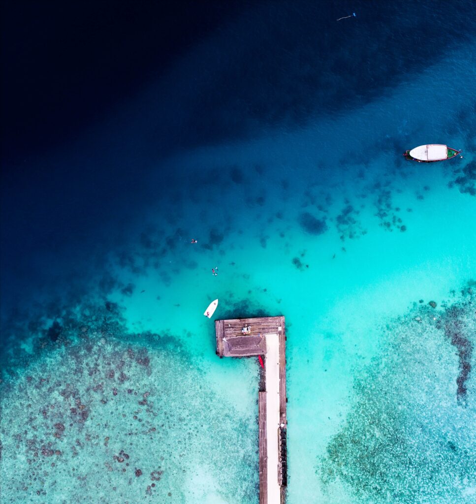 Aerial view of pier over vibrant turquoise ocean with coral reefs and boats calm adventure wallpaper