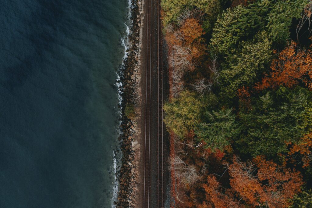 Aerial view of railway along rugged coastline with deep blue water and autumn forest foliage background Wallpaper
