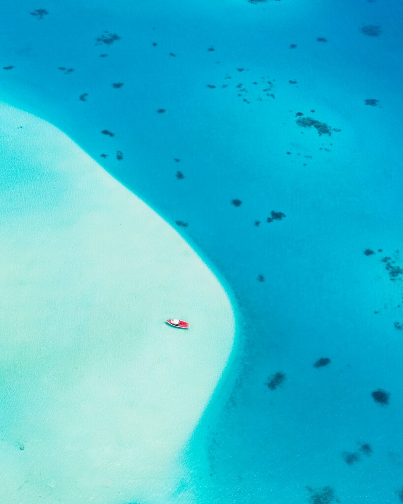 Aerial view of vibrant red boat drifting on clear turquoise waters near sandy shoreline wallpaper