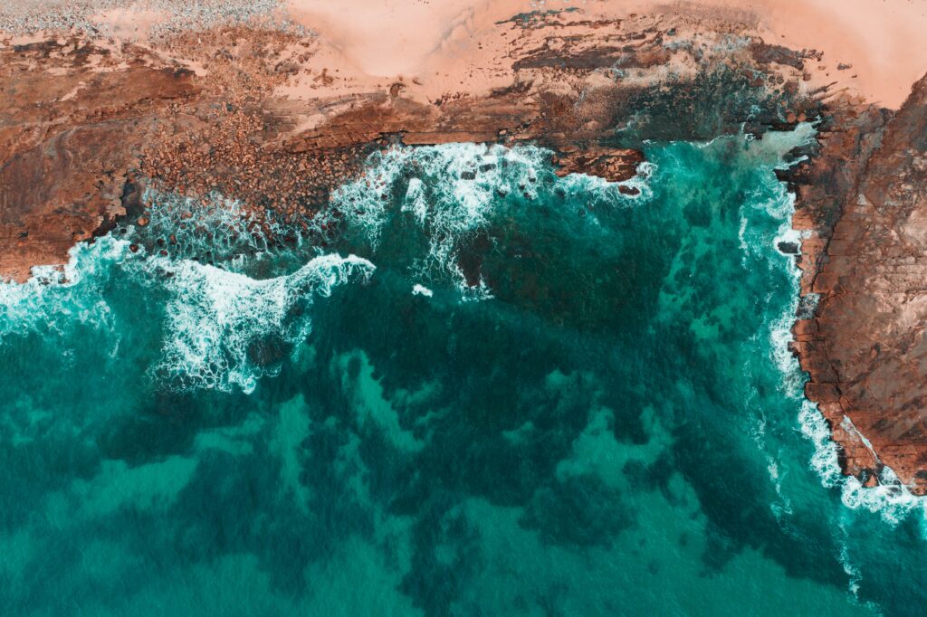 Aerial view of rugged coastline with turquoise waves crashing on rocky sandy shores wallpaper background