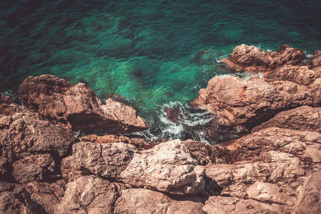 Aerial view of rugged coastal rocks meeting clear turquoise sea with vibrant natural textures Wallpaper