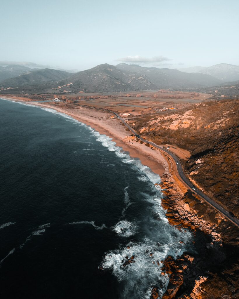 Aerial view of rugged coastline with winding road rolling hills golden sands and distant mountains Wallpaper
