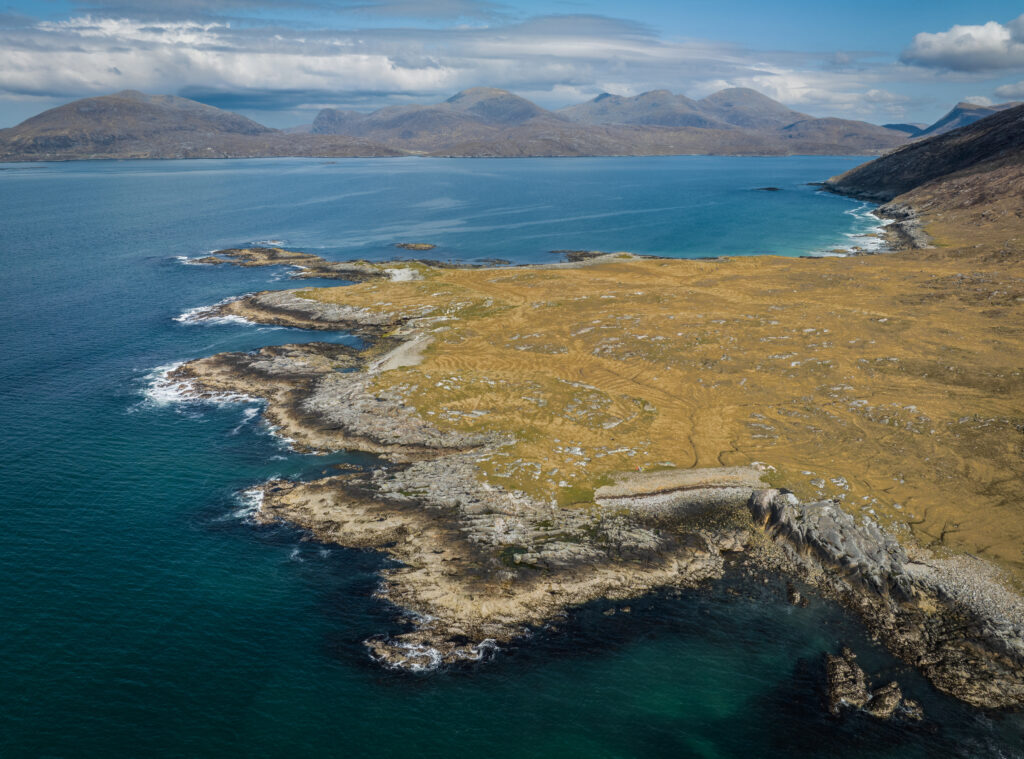 Aerial view of rugged island coastline with rocky shores golden grass turquoise sea and mountains Wallpaper