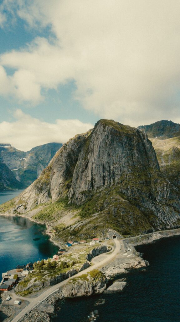 Aerial view of rugged coastal mountain island with winding roads small houses and blue waters Wallpaper