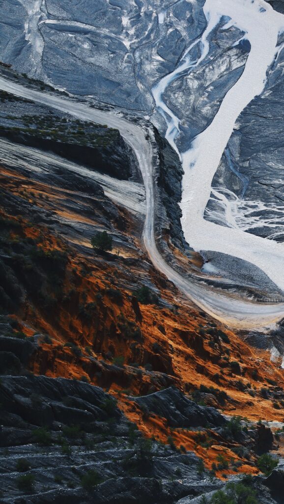 Aerial view of rugged mountains with orange earth blue-gray rocks winding river and paths wallpaper