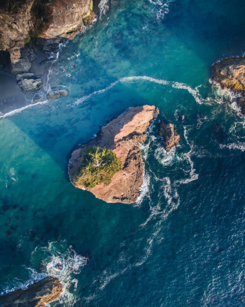 Aerial view of rugged rocks and vibrant blue sea with white waves crashing against shore Wallpaper