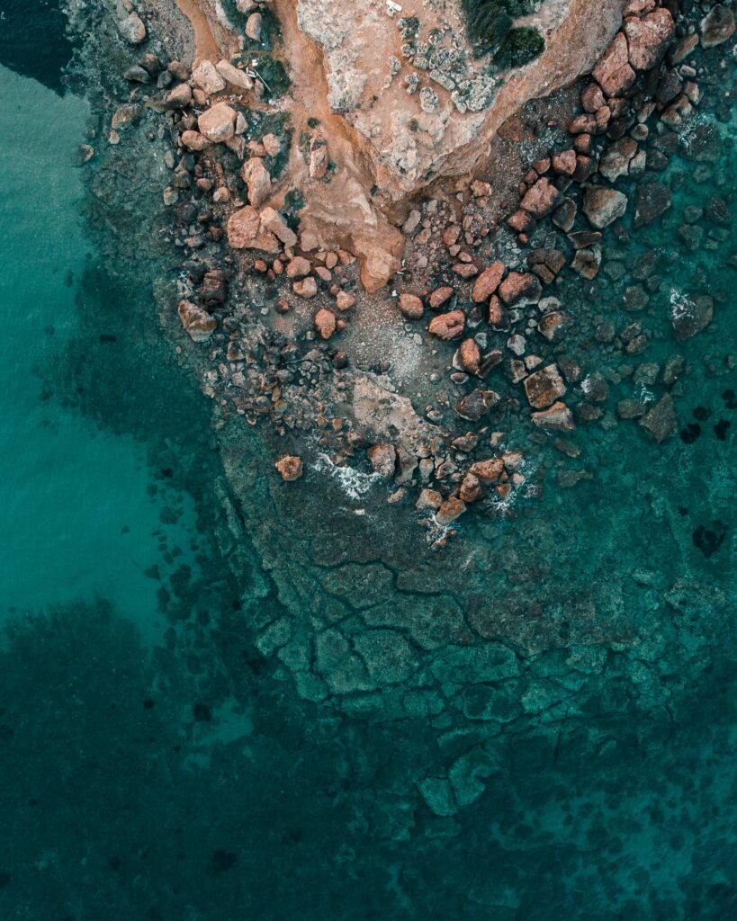 Aerial view of rugged rocky coastline meeting clear turquoise sea natural scenic wallpaper background